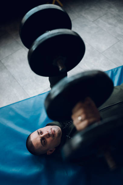istock Man lying on the mat in the gym and training with dumbbell 1370984410