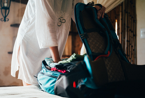 An unrecognizable young woman packs a backpack in the bedroom