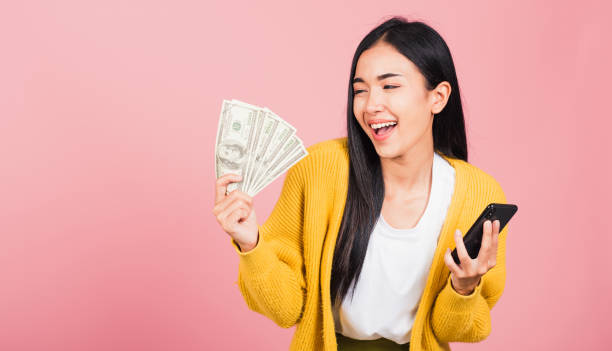 woman shopper smiling standing excited holding online smart mobile phone and dollar money banknotes stock photo