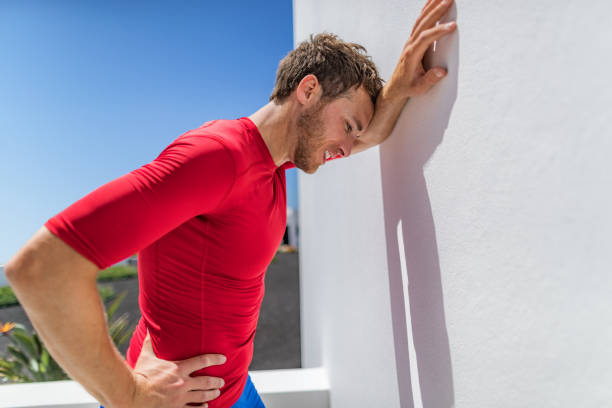 Tired athlete runner man exhausted leaning on wall of fatigue breathing hard after difficult exercise. Fitnes person sweating of sun stroke, migraine, heat exhaustion muscle back pain or cramps. stock photo