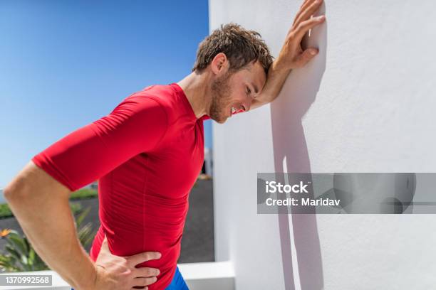 Tired Athlete Runner Man Exhausted Leaning On Wall Of Fatigue Breathing Hard After Difficult Exercise Fitnes Person Sweating Of Sun Stroke Migraine Heat Exhaustion Muscle Back Pain Or Cramps Stock Photo - Download Image Now