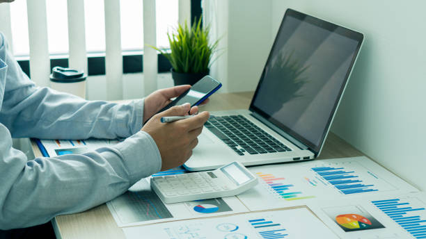 istock Businessman holding a mobile smartphone work on a laptop computer Analyzing, calculating, graphing, business data in the office, reviewing profit reports. business strategy ideas 1371000154