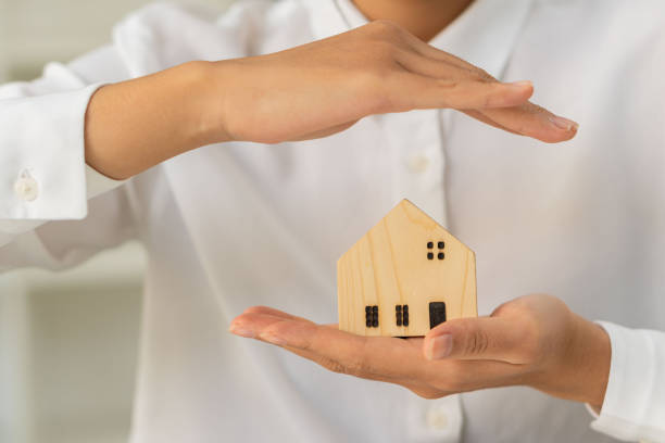 Asian woman's hand holds a small house model and folds her arms in defense above insurance concept. real estate and foster home care and family concepts. stock photo