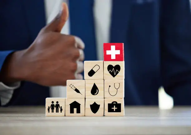 Photo of Shot of an unrecognisable businessman assembling wooden blocks with insurance related symbols on them and showing thumbs up