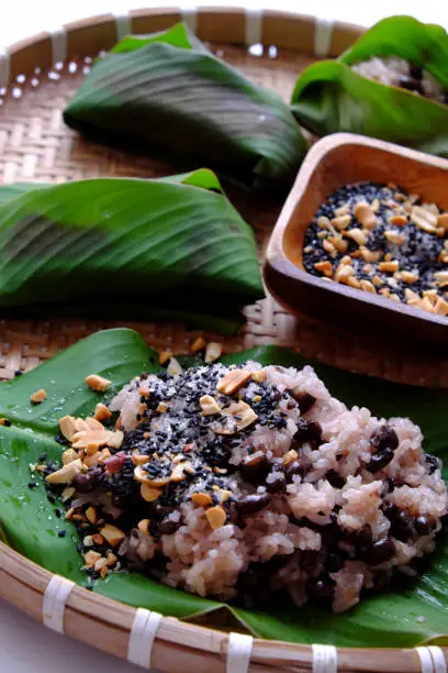 Top view Vietnamese homemade black bean sticky rice with sesame salt for cheap and quick breakfast in green leaf on bamboo basket on white background