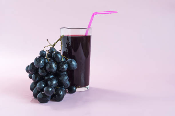 istock A vine with black berries and a transparent glass with grape juice on a light background. 1371006461