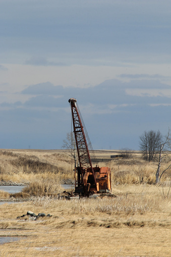 Outdoor industrial  image of an old rusted mobile crane abandoned in a pasture of dry grass.