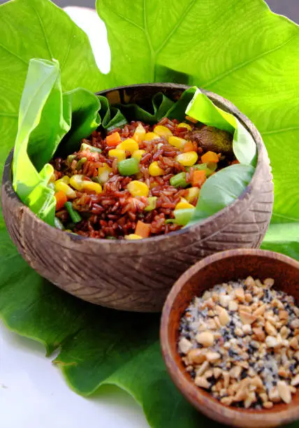 Vietnamese cuisine from red rice, delicious and nutrition rice dish for lunch, homemade food rich nutritious in coconut shell bowl with sesame salt on green leaf background