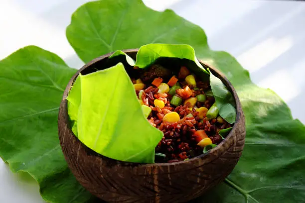 Vietnamese cuisine from red rice, delicious and nutrition rice dish for lunch, homemade food rich nutritious in coconut shell bowl with sesame salt on green leaf background