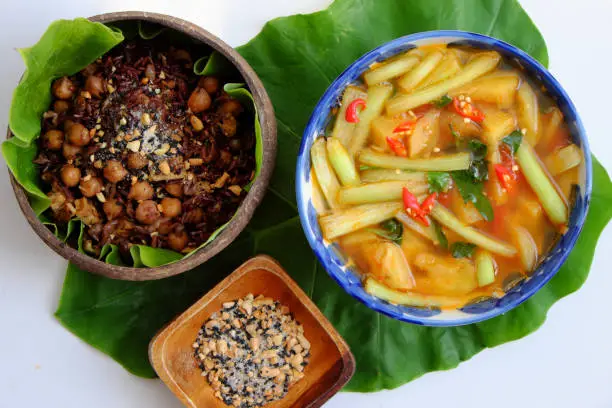 Vietnamese cuisine from red rice, delicious and nutrition rice dish for lunch, homemade food rich nutritious in coconut shell bowl with sesame salt on green leaf background