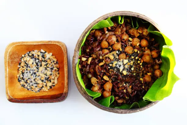 Vietnamese cuisine from red rice, delicious and nutrition rice dish for lunch, homemade food rich nutritious in coconut shell bowl with sesame salt on green leaf background