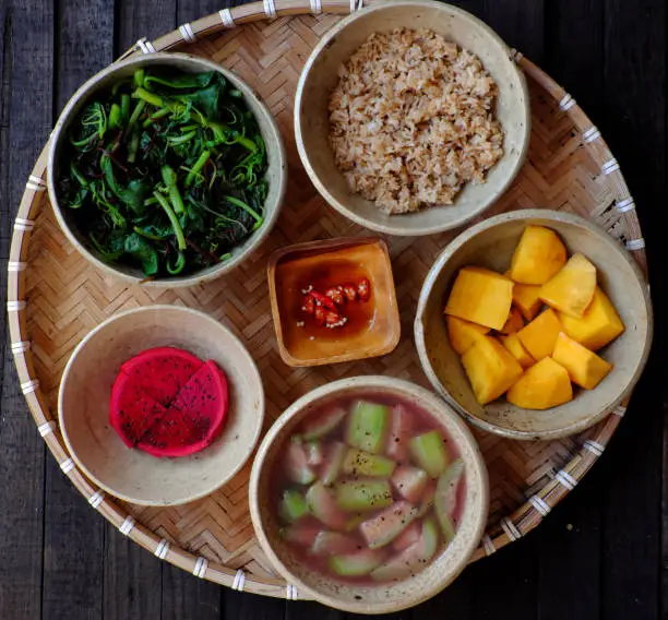 Frugal meal with vegetarian food, boiled vegetable, melon soup, fried rice, mango, dragon fruit, top view healthy tray for food on black wooden for lunch