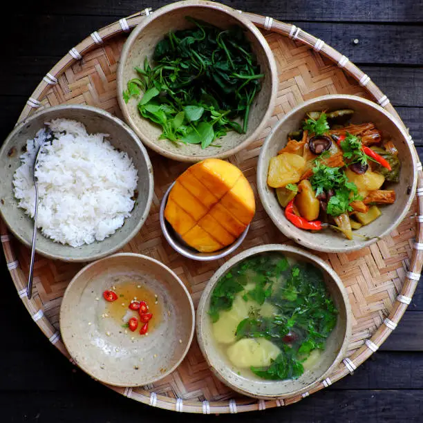 Top view Vietnamese daily meal for lunch, tray of rice dish with boiled sweet potato buds, pineapple soup, tofu skin, pineapple, mushrooms cook with sauce , vegan menu with non meat good for health