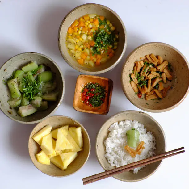 Top view Vietnamese daily meal for lunch time, tray of rice dish with melon, soup bowl from carrot, corn, potato, tofu skin fried, pineapple, sauce, vegan menu with non meat so good for health