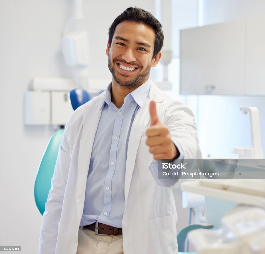 Portrait of a young dentist showing thumbs up in his consulting room In the market for a new smile? I'm your man Dentist Stock Photo