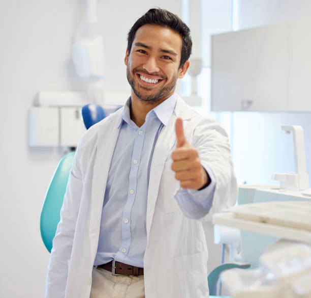 портрет молодого стоматолога, показывающего большие пальцы вверх в своей консультационной комнате - dentist asian ethnicity portrait male стоковые фото и изображения
