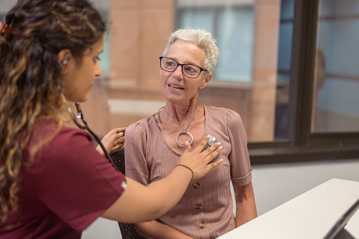 A mature adult woman has her heart checked with a stethoscope while at a medical appointment.