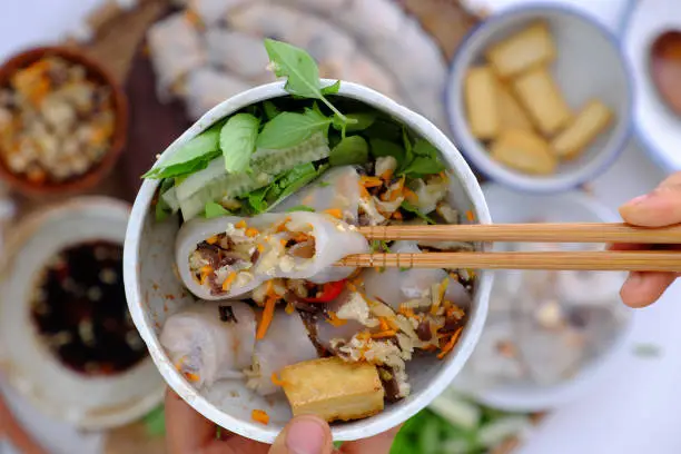 Top view people have breakfast at home with homemade vegan Vietnamese rice noodles roll, close up hand hold bowl of stuffed pancake dish on food background so delicious for veg