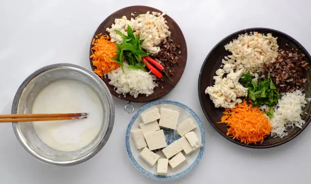 Top view raw material ready to cook homemade rice noodles roll, vegan ingredient as wood ear mushroom, carrot, rice batter, tofu that chopped on white background, Vietnamese popular dish