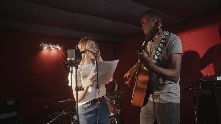 Guy and woman record acoustic song in semi-dark studio