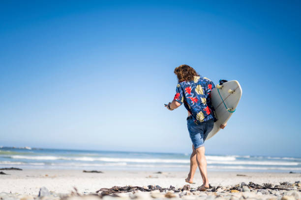 istock Male with surfboard on beach walking checking his phone 1371019090