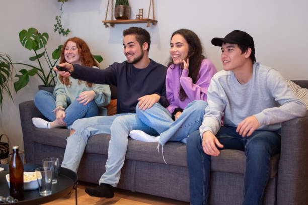 istock Smiling friends sitting on sofa at home and watching television 1371021389