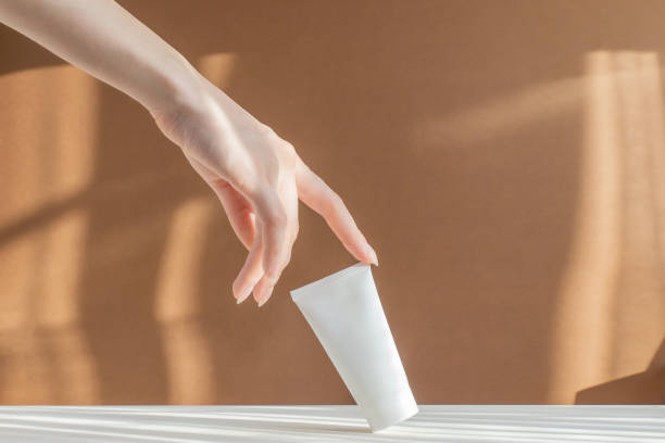 Woman's finger touches mock up of cream tube. Brown and white background with rays of sunlight. Packaging for cosmetics. Concept of skin care and advertising Woman's finger touches mock up of cream tube. Brown and white background with rays of sunlight. Packaging for cosmetics. Concept of skin care and advertising. white plastic tube stock pictures, royalty-free photos & images