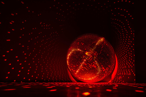 Disco ball reflecting red light in a dark hall for discos. Copy space.