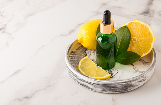 bleaching, rejuvenating agent with lemon extract in a glass bottle with a pipette on a plaster plate and a marble background with fruit fruits