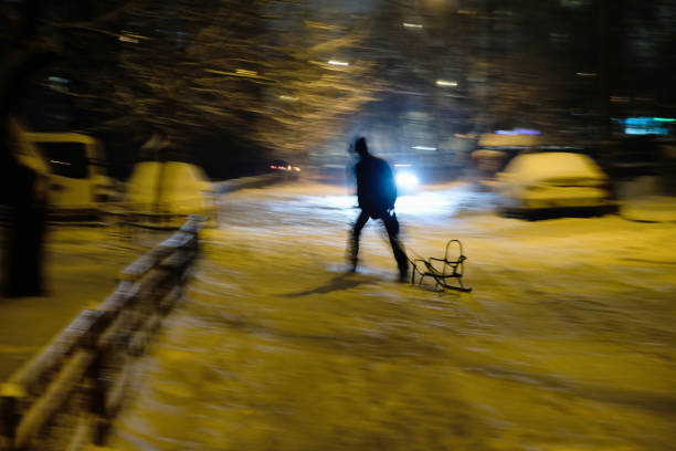 A male silhouette pulls an empty sled into a night blizzard in Ukraine.  Slow shutter speed photography of people in motion. Poor visibility.