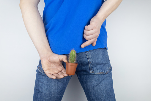 Concepto. Un hombre sostiene un cactus como símbolo de dolor rectal. Venas varicosas de la parte inferior del intestino. Dolor en el recto, hemorroides y dolor en el sistema excretor del cuerpo. Proctología photo