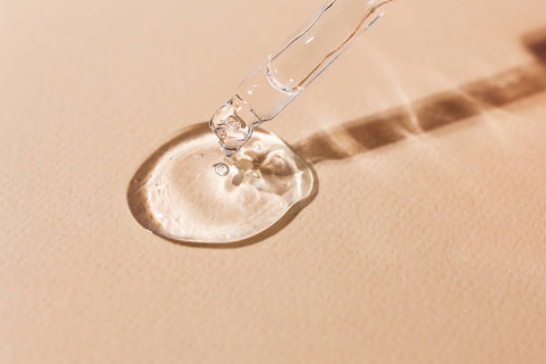 Transparent body serum flowing from a glass pipette front view.Cosmetic product close-up on a beige background Transparent body serum flowing from a glass pipette front view.Cosmetic product close-up on a beige background. serum sample stock pictures, royalty-free photos & images