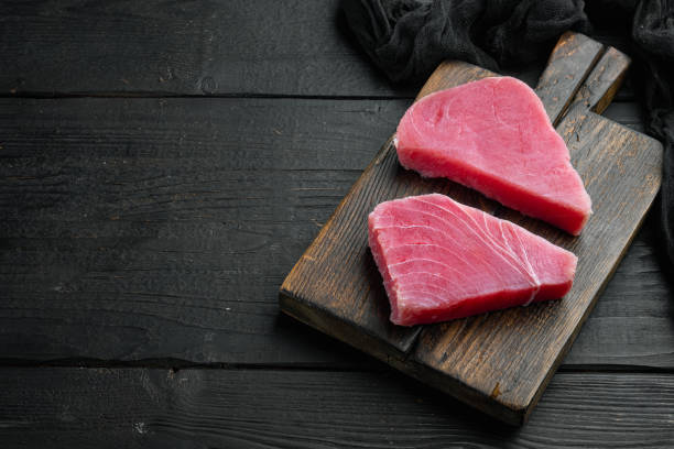 pezzi di tonno crudo, su tagliere di legno, su fondo di legno nero, con copyspace e spazio per il testo - tuna seared tuna steak prepared ahi foto e immagini stock