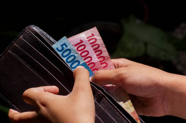 un bambino asiatico prende i soldi indonesiani dal portafoglio. concetto di risparmio e donazione - indonesian currency foto e immagini stock