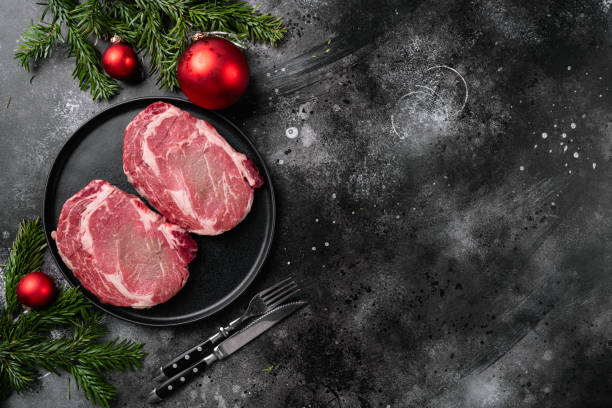 クリスマスと新年にコショウとハーブと生のリブアイビーフステーキ, 黒い暗い石のテーブルの背景に, トップビューフラットレイ, テキストのためのコピースペース付き - strip steak ストックフォトと画像