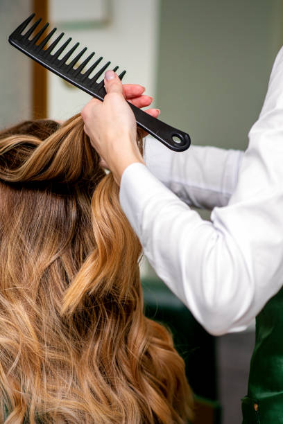 A female hairdresser is combing the long brown hair of a young woman at a parlor. A female hairdresser is combing the long brown hair of a young woman at a parlor hair length stock pictures, royalty-free photos & images