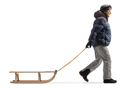 Full length profile shot of a mature man in winter clothes pulling a sled isolated on white background