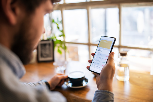 Young man tracking finance on mobile app while drinking coffee.