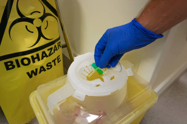 Gloved hand putting green needle sharp into biohazard safety bin Disposal of sharps in containers is common in hospital settings following phlebotomy, referred to as taking blood by non health professionals biological warfare stock pictures, royalty-free photos & images