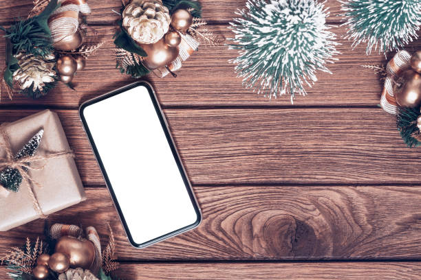istock Mockup smartphone with blank white screen, new year gift box with Xmas pine tree model, christmas ornaments on wood background, top view, place for your artwork 1371042638