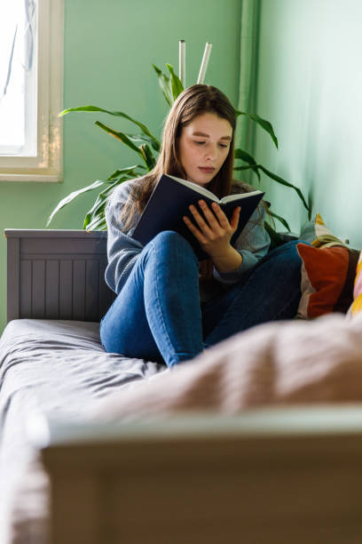 istock Young woman sitting on her bed and writing in her diary 1371044932