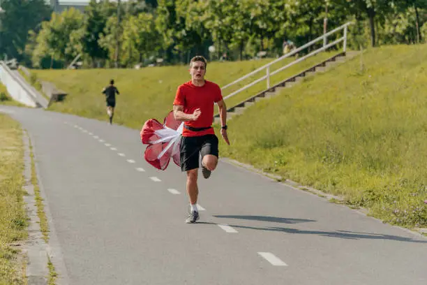 Photo of Male athlete wearing a red t-shirt is running with a parachute in the park