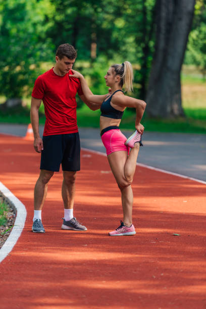 istock Young male athlete supporting his young female partner while she is stretching her legs after running on a race track. 1371045958