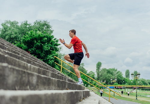 Fit male athlete performing stairs workout, running up climbing stairs performing outdoor track cardio.