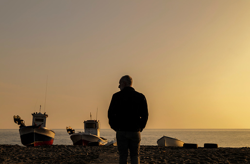 Rear view of adult man on beach with fishing boat during sunset. Almeria, Spain