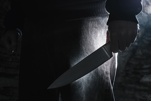 Dark photo of a man holding a big knife, crime concept.