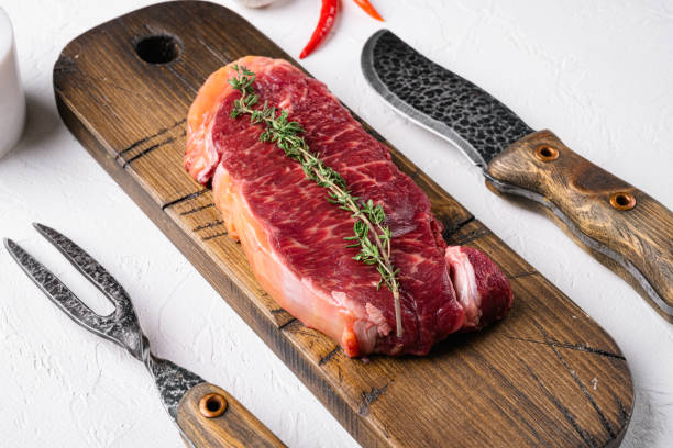 白い石のテーブルの背景に生のストリップロースステーキ - strip steak ストックフォトと画像