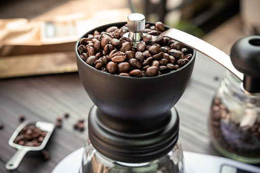 Coffee beans roasted in a manual coffee grinder on a wooden table, drip coffee maker