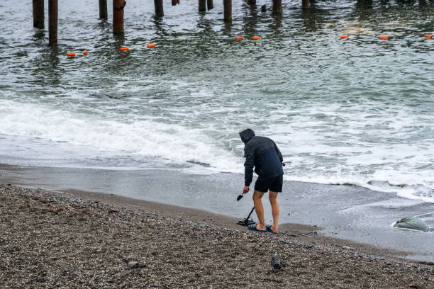 hombre con detector de metales en la playa del mar - shingle beach fotografías e imágenes de stock