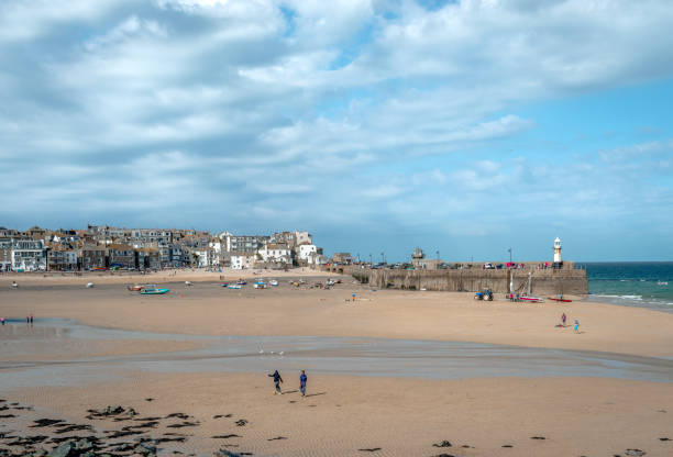Panoramic view of the St Ives harbor, Cornwall, England, UK. Low tide, dramatic sky, unidentified people play at the beach.